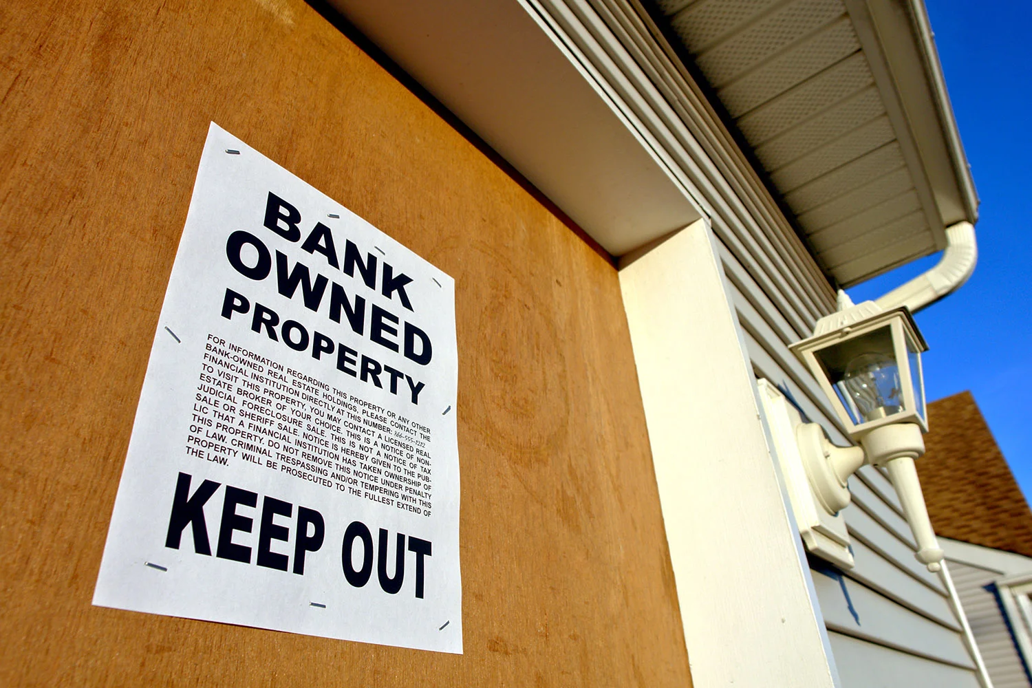 Real estate lender bank owned keep out sign notice posted on a boarded up house